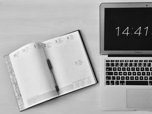 Calendar planner next to a computer showing the time.