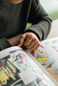 Young student looking at a book with cartoons and pictures.
