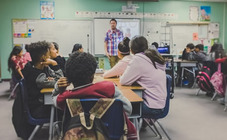 Teacher standing in front of a class, students sitting in desks.